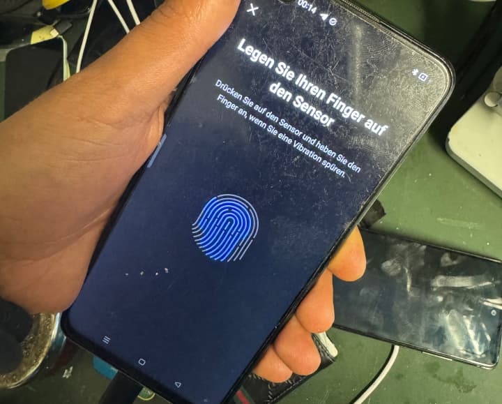 Ein funktionstüchtiges Smartphone, das einen Fingerabdrucksensor auf dem Bildschirm anzeigt, gehalten in der Hand eines Technikers.