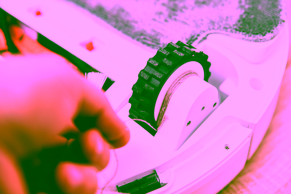 Eine Hand entfernt verhedderte Haare aus dem Rad eines Staubsaugerroboters.