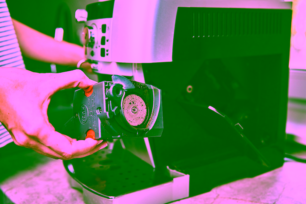 Eine Person nimmt die Brühgruppe aus einer Kaffeemaschine zur Reinigung oder Reparatur des Kaffeevollautomaten heraus.