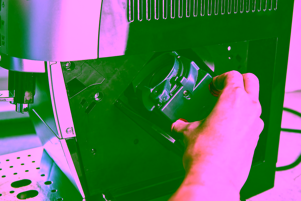 Die Hand einer Person nimmt die Brüheinheit zur Reinigung oder Wartung aus dem Inneren einer Kaffeemaschine heraus.